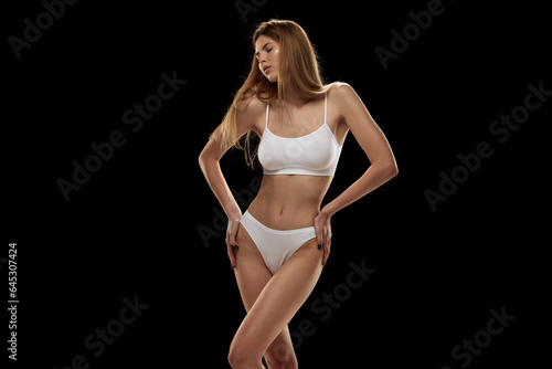 Canvas Print Young sensual woman with slender legs posing in white color lingerie isolated over black background