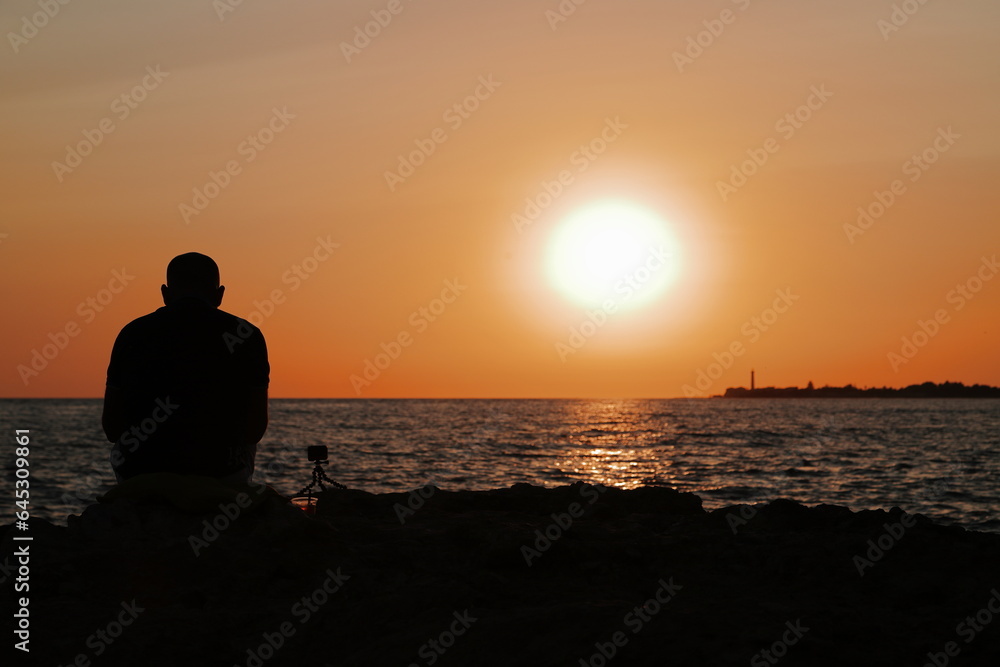 Signore che guarda e filma il tramonto da una scogliera a Marina di Ragusa
