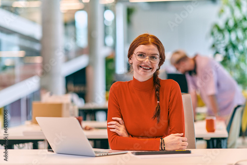 In a modern startup office, a professional businesswoman with orange hair sitting at her laptop, epitomizing innovation and productivity in her contemporary workspace.