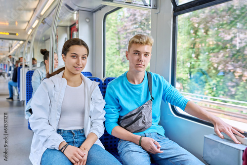 Teenage guy and girl commuter train passengers sitting together, smiling, looking at camera © Valerii Honcharuk