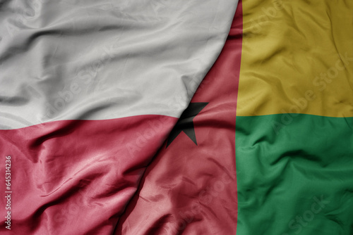 big waving national colorful flag of poland and national flag of guinea bissau .