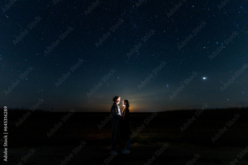 Fototapeta premium silhouettes of a couple in love at night against the backdrop of the night starry sky, romantic date