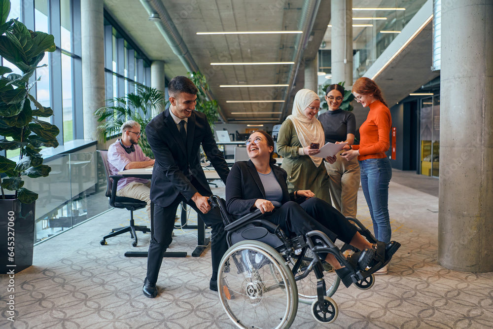 A diverse group of business colleagues is having fun with their wheelchair-using colleague, demonstrating their attention and inclusivity in the workplace