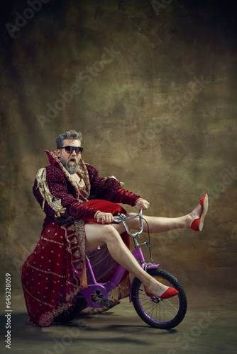 Photography Man, medieval royal person in female dress and shoes riding little bike over vintage background