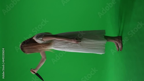 Full-size side view vertical green screen, chroma key video of a posessed female, woman figure, ghost, poltergeist, zombie raising, pulling out a knife. Hair is covering her face. Chroma key. photo