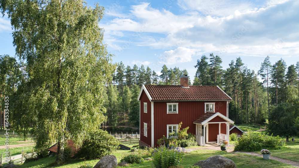 a typical red and white swedish house in smalland. green meadow in foreground
