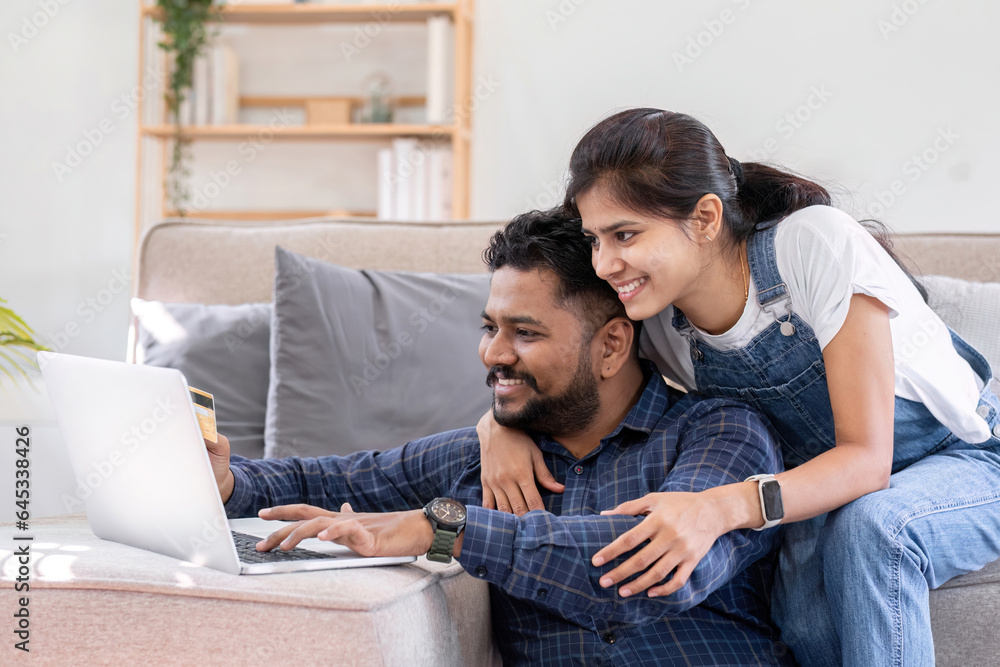 Cropped view of young woman hugging husband while using laptop on sofa in living room Cropped view of young woman hugging husband while using laptop on sofa in living room