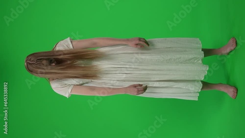 Full-size vertical green screen, chroma key video of a posessed female, woman figure, ghost, poltergeist, zombie standing with her arms down, staggering, hunched. Hair is covering her face. Chroma key photo