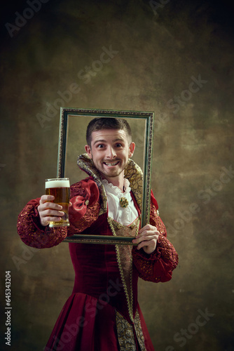 Canvas Print Medieval royal person, prince in female dress holding picture frame and drinking beer against dark green background