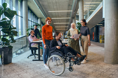 A diverse group of business colleagues is having fun with their wheelchair-using colleague, demonstrating their attention and inclusivity in the workplace © .shock