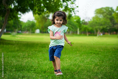 Cheerful and carefree little indian girl child running at summer park or garden.