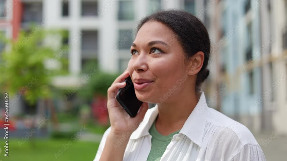 Ethnic American Contented Charming Lady Talking on the Smartphone with Friends, Smiling, and Laughing with Cute Smile, Outside. African American Girl Makes an Online Order on Her Smartphone Outside Ethnic American Contented Charming Lady Talking on the Smartphone with Friends, Smiling, and Laughing with Cute Smile, Outside. African American Girl Makes an Online Order on Her Smartphone Outside