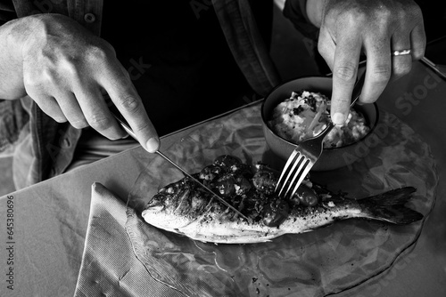 Man eating grilled dorada fish and rice with celery root puree in a seaside provencal restaurant in Camargue, France. Simple healthy delicious local food. Food background. Black white photo. photo