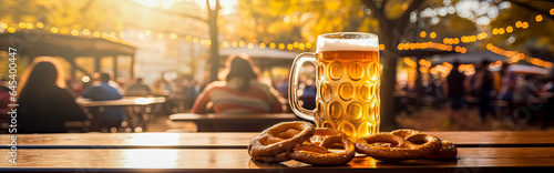 mug of cold beer and tasty fresh brezels on a wooden table at a Biergarten at sunset with blurred background photo