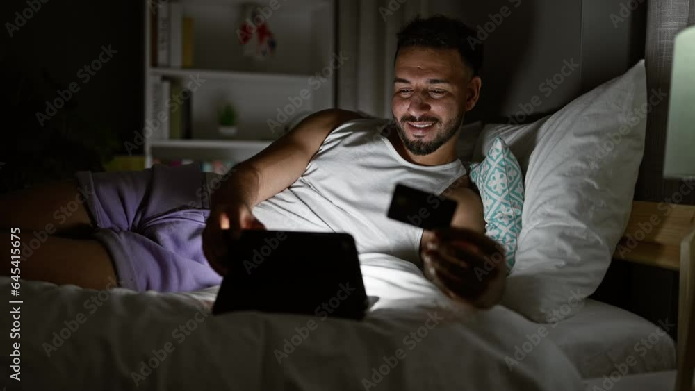 Young arab man shopping with laptop and credit card sitting on bed at bedroom Young arab man shopping with laptop and credit card sitting on bed at bedroom