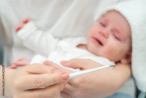 Mother calms crying baby while checking fever. Concept of sick baby