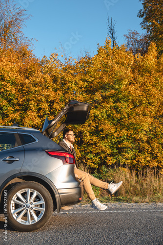 A man sits in the trunk of his car and enjoys the autumn sun as he basks in it