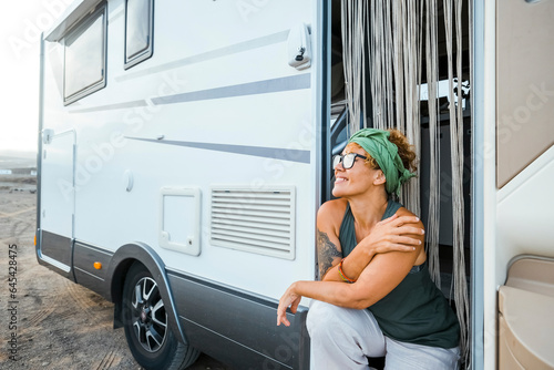 Adventure travel lifestyle in modern camper van. One solo traveler nomadic woman sitting on the door outside her motorhome. Alternative travel and vanlife lifestyle people enjoying freedom life