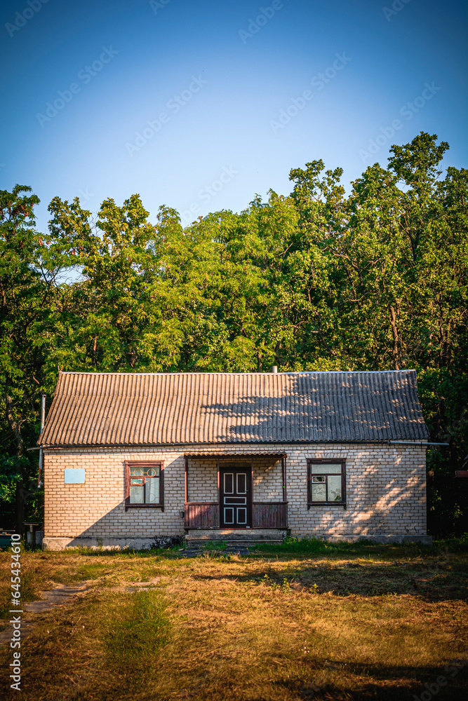 old cozy white brick house with a window, against a background of green trees, during the golden hour old cozy white brick house with a window, against a background of green trees, during the golden hour