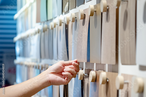 Designer hand picking wood samples board from material swatch wall display in material library. Choosing wooden laminate texture in beige tone collection for interior architecture or furniture design photo