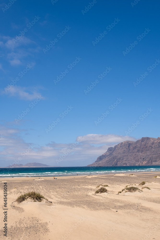 White sand beach. Famara beach. Turquoise water, island of La Graciosa and cliffs in the background. Sky with big white clouds. Caleta de Famara.Lanzarote, Canary Islands, Spain.