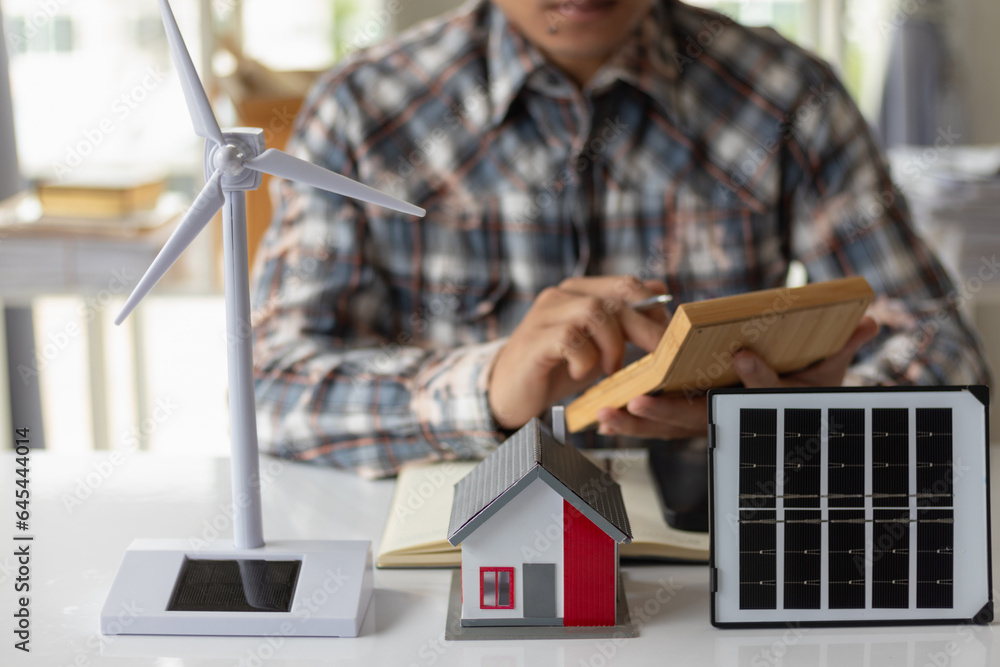 On desk of engineers lay model of house And solar panels to use in planning installation of solar panels to  house in order to get most cost effective energy from installing solar panels.