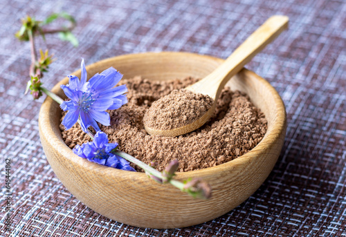 Ground chicory root in a wooden cup and chicory flowers on a rustic wooden background. Alternative medicine. Healthy drinks. chicory drink photo