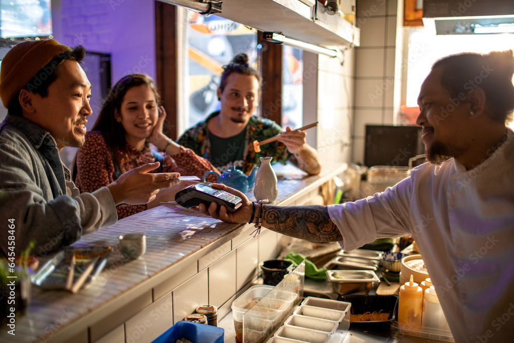 Diverse group of friends paying for their meal with a credit card in a sushi restaurant or bar Diverse group of friends paying for their meal with a credit card in a sushi restaurant or bar
