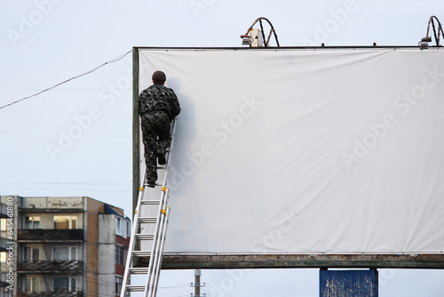 a person on a ladder painting a white sign or banner. copy space and mock up.