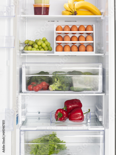 Fridge open with food inside. Eggs and fresh vegetables.