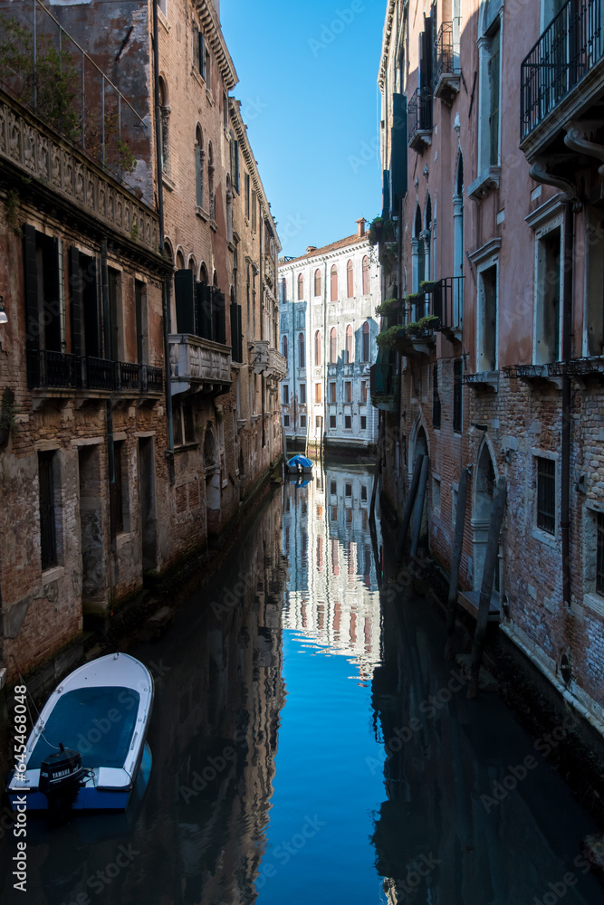 Una piccola barca ormeggiata in un canale di Venezia in una giornata di sole con i palazzi che si riflettono nell'acqua