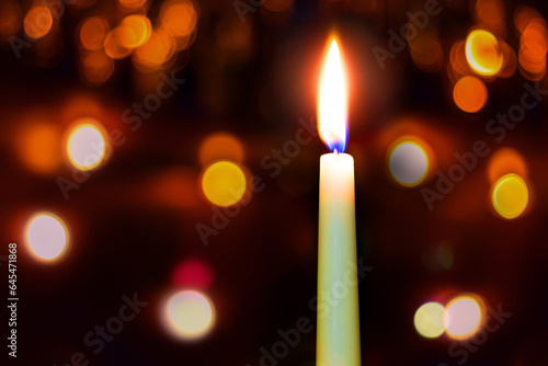 Candle burns on a dark background with bright bokeh