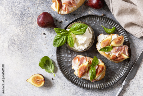 Italian appetizer recipe. Toast or bruschetta with bacon and figs, cream cheese and honey on a gray stone background. View from above. Copy space.