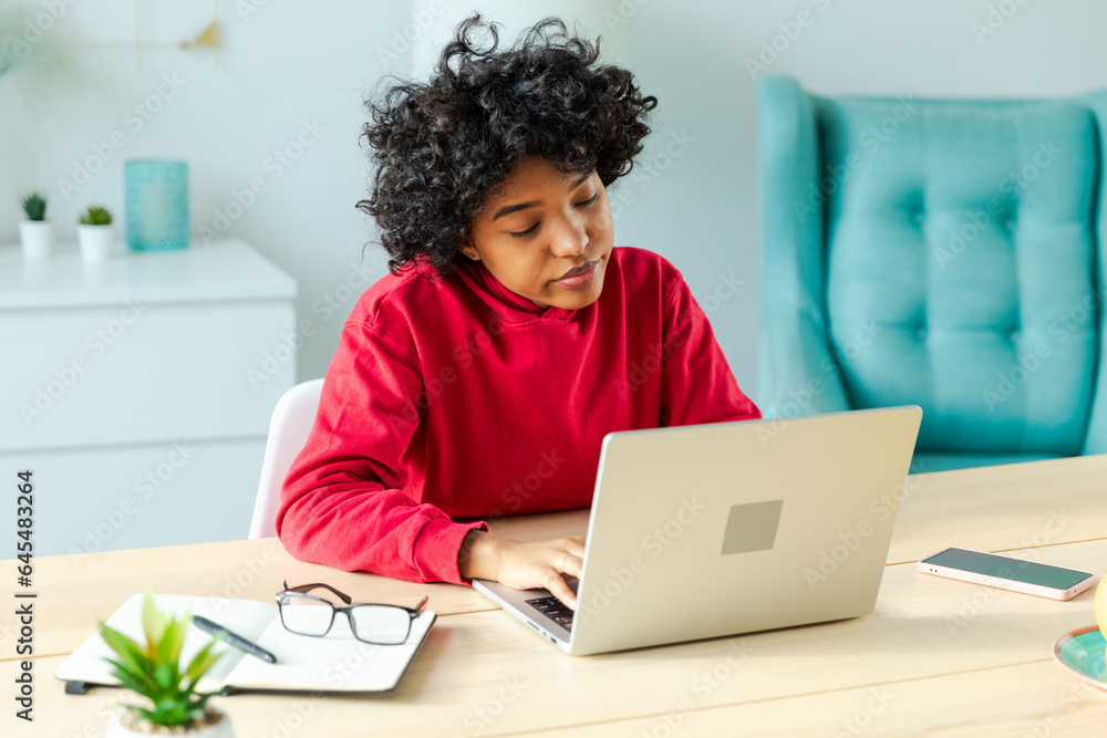African american girl using laptop at home office looking at screen typing chatting reading writing email. Young woman having virtual meeting online chat video call conference. Work learning from home African american girl using laptop at home office looking at screen typing chatting reading writing email. Young woman having virtual meeting online chat video call conference. Work learning from home