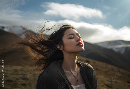 Woman with eyes closed and hair blown by the wind breathes deeply at the top of the mountain. Meditation, introspective woman