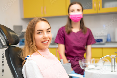 Happy young woman patient smilling sitting in medical chair at dental clinic. Stomatologist standing behind the patient.
