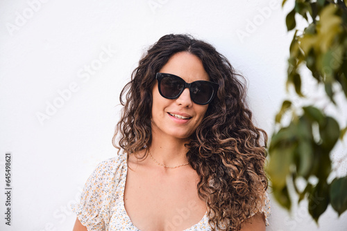 Young and stylish 26 year old beautiful girl with brown hair posing smiling in front of a white wall.