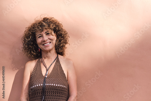 mature woman about 55 years old posing in front of a light brown wall