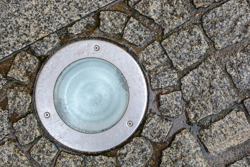 Close-up of a stone pavement with an illuminating round lamp, wet from the rain. Pavement background texture with geometric pattern