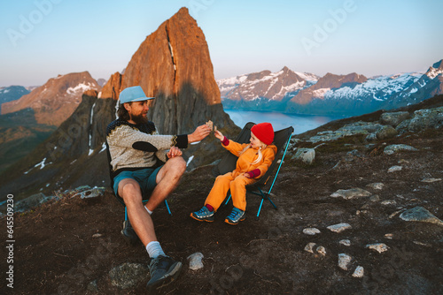 Father with daughter on picnic outdoor hiking in Norway mountains together happy family travel lifestyle active vacations man with kid sitting in camping chairs eating snacks Father's day holiday photo