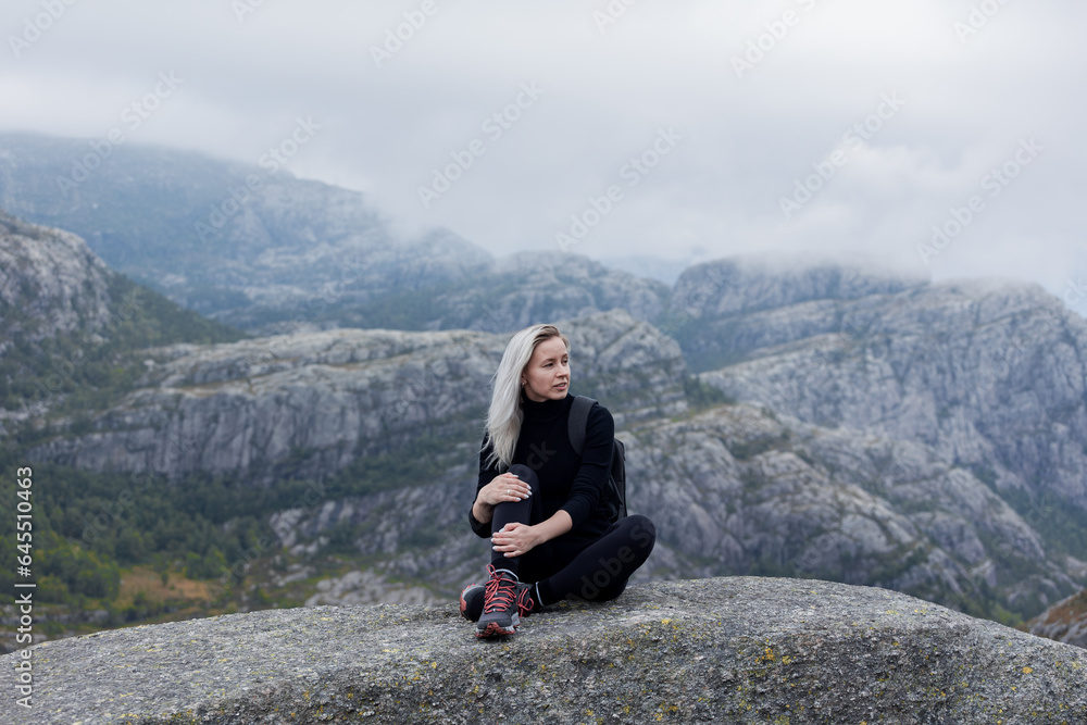 a girl with a backpack sitting on the rock in the mountains on a hike in Norway on fjord