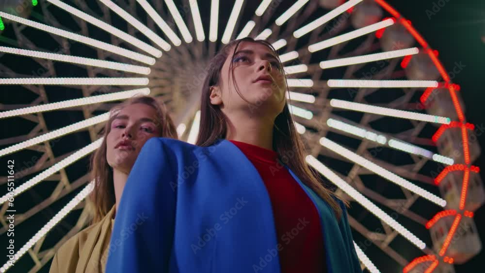 Gorgeous girls look camera at blinking ferris wheel closeup. Trendy models rest Gorgeous girls look camera at blinking ferris wheel closeup. Trendy models rest