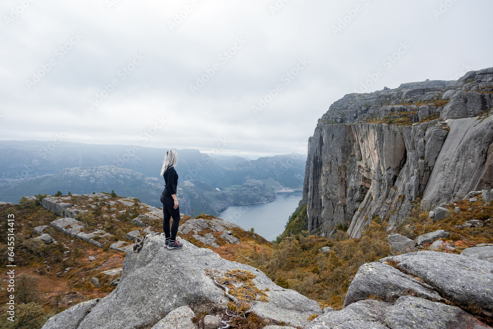 a girl standing on the edge of the cliff in the mountains on a hike in Norway on fjord