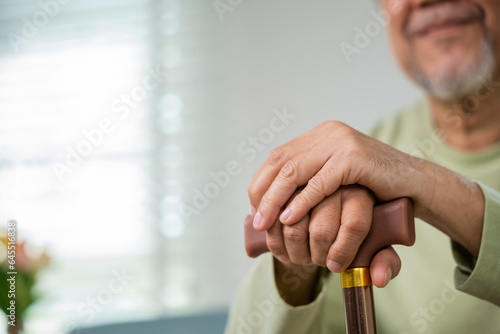 Close up hands of Asian Elderly hand holding handle of cane, senior disabled man holding walking stick, Old man sitting resting at home hold wooden walking cane, International Day for the Elderly