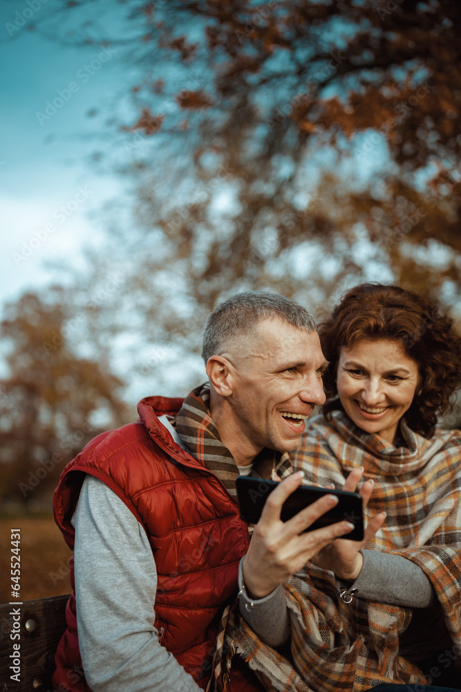 Fototapeta premium smiling romantic family in park using smartphone