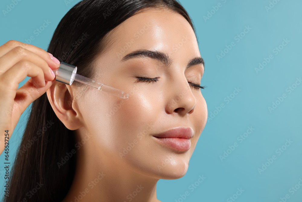 Beautiful young woman applying serum onto her face on light blue background, closeup. Space for text Beautiful young woman applying serum onto her face on light blue background, closeup. Space for text