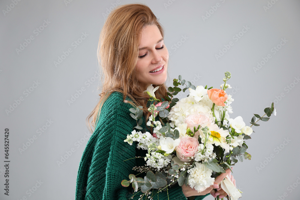 Beautiful woman with bouquet of flowers on grey background