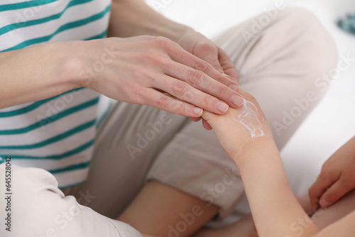 Mother applying ointment onto her daughter's hand on bed, closeup