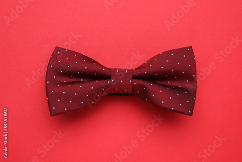 Stylish burgundy bow tie on red background, top view