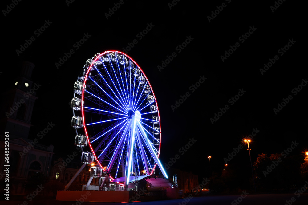 Beautiful glowing Ferris wheel on city street at night. Space for text